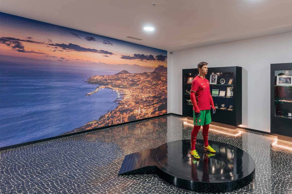 Soccer player statue in a room with a cityscape wall mural and display cases.