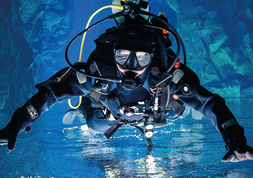 Scuba diver in full gear underwater, swimming near rocky formations.
