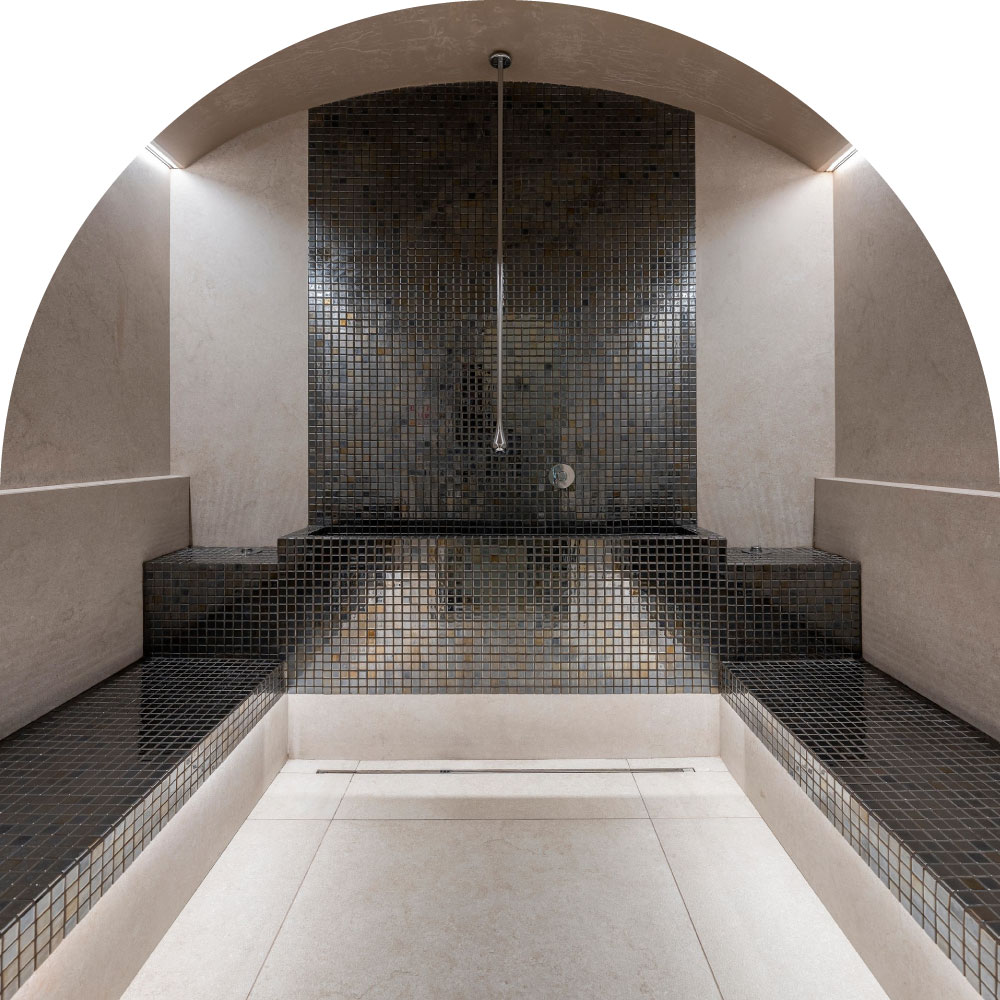 Tiled steam room with arch ceiling and benches, central shower head above mosaic wall.
