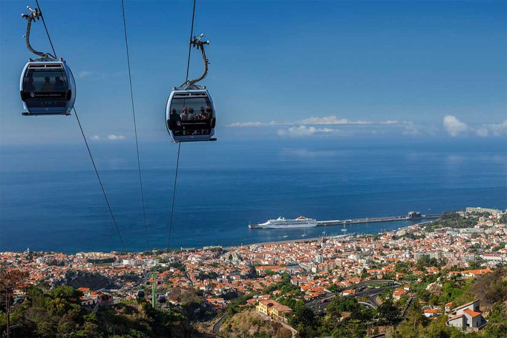 Cable cars over a seaside city with a cruise ship in the harbor.