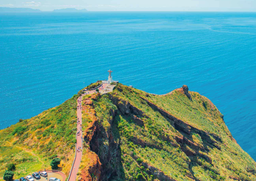Hill with a path and statue overlooking the sea, clear sky above.