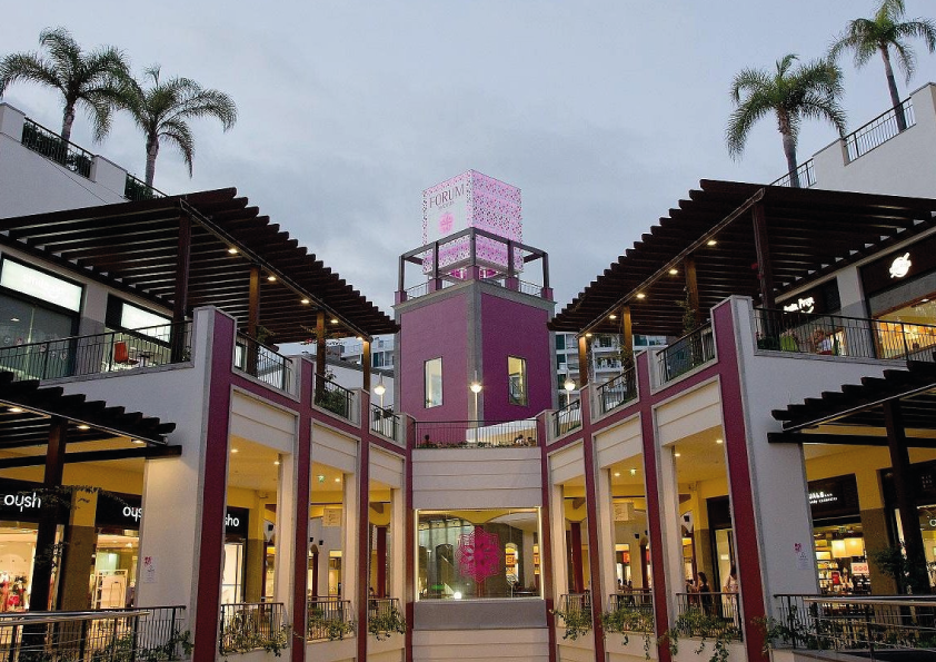 Shopping center with a pink tower and palm trees at dusk.
