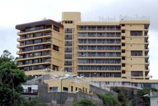 Tall beige hotel building with balconies on a hillside.