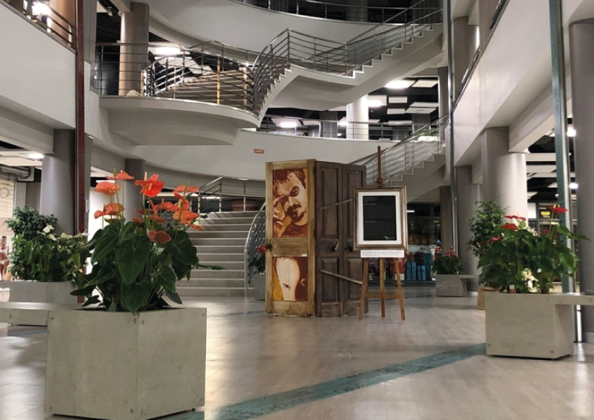 Spiral staircase in a modern atrium with plants and a framed artwork display.