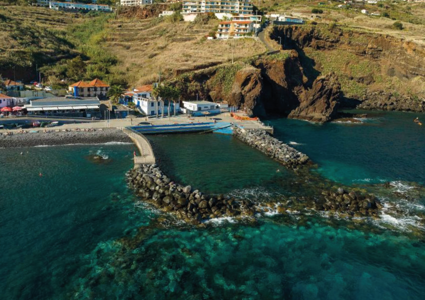 Aerial view of a coastal village with cliffs and clear blue water.