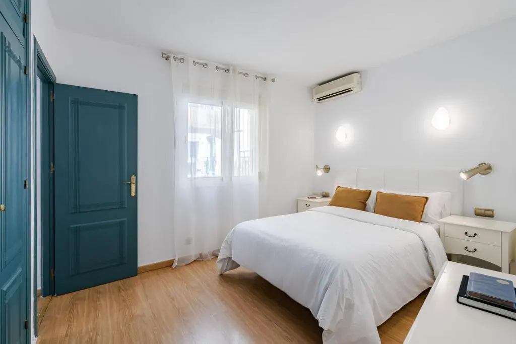 Habitaci&oacute;n minimalista con tonos blancos y azules, cama doble y ventana.