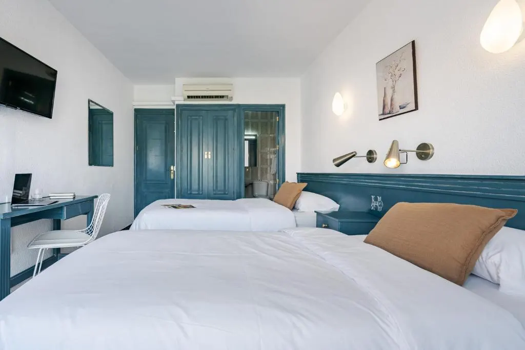 Habitaci&oacute;n con dos camas, escritorio, TV y decoraci&oacute;n en tonos azules.