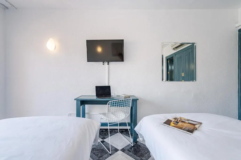 Habitaci&oacute;n con TV, escritorio azul y dos camas blancas.