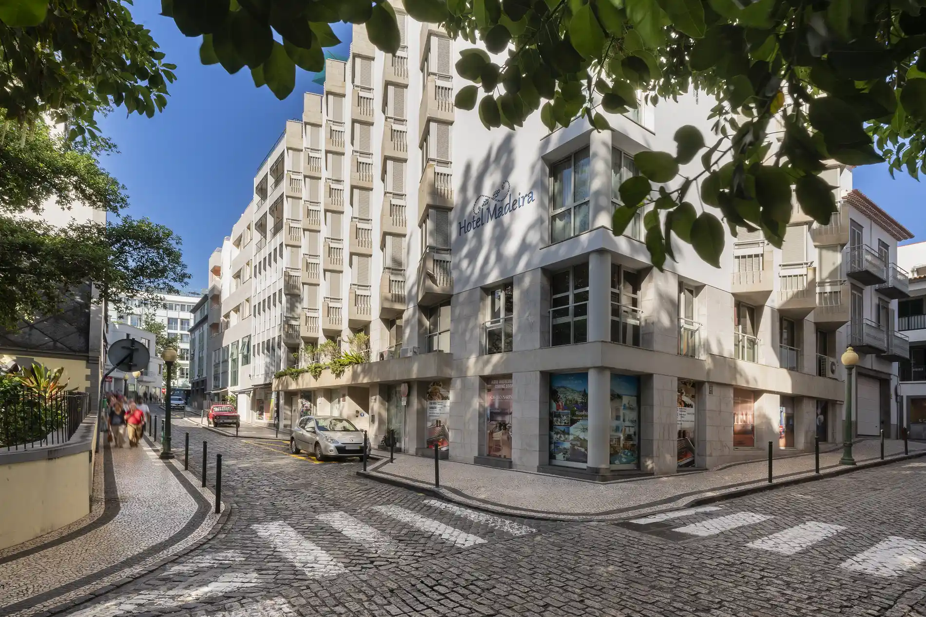 Cobblestone street with buildings and greenery under a clear blue sky.