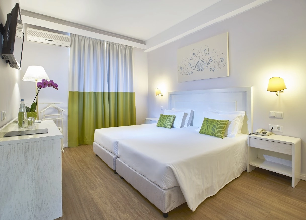 Modern hotel room with twin beds, green decor, and a wall-mounted TV.