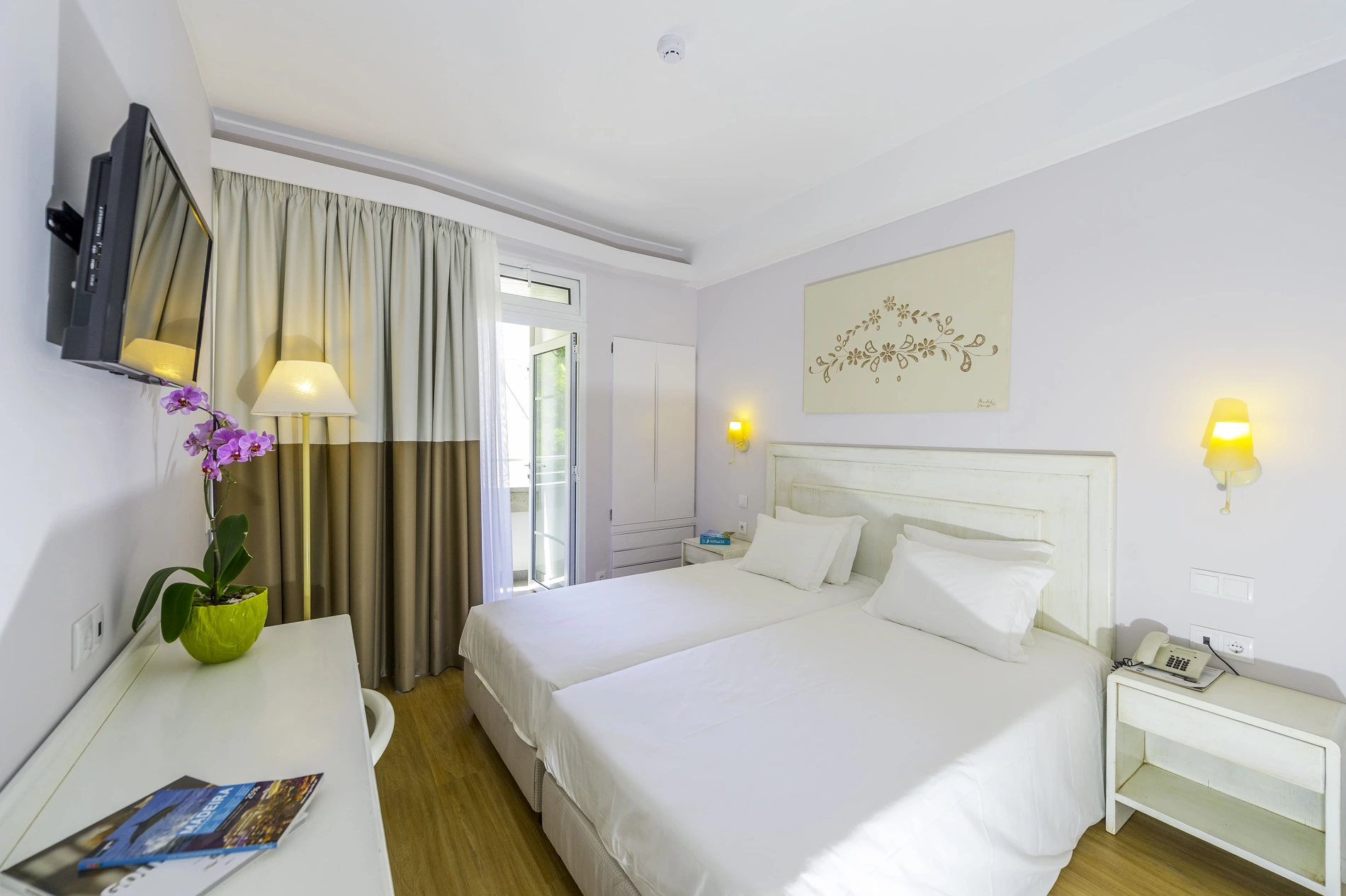 Hotel room with twin beds, TV, orchid plant, and balcony.