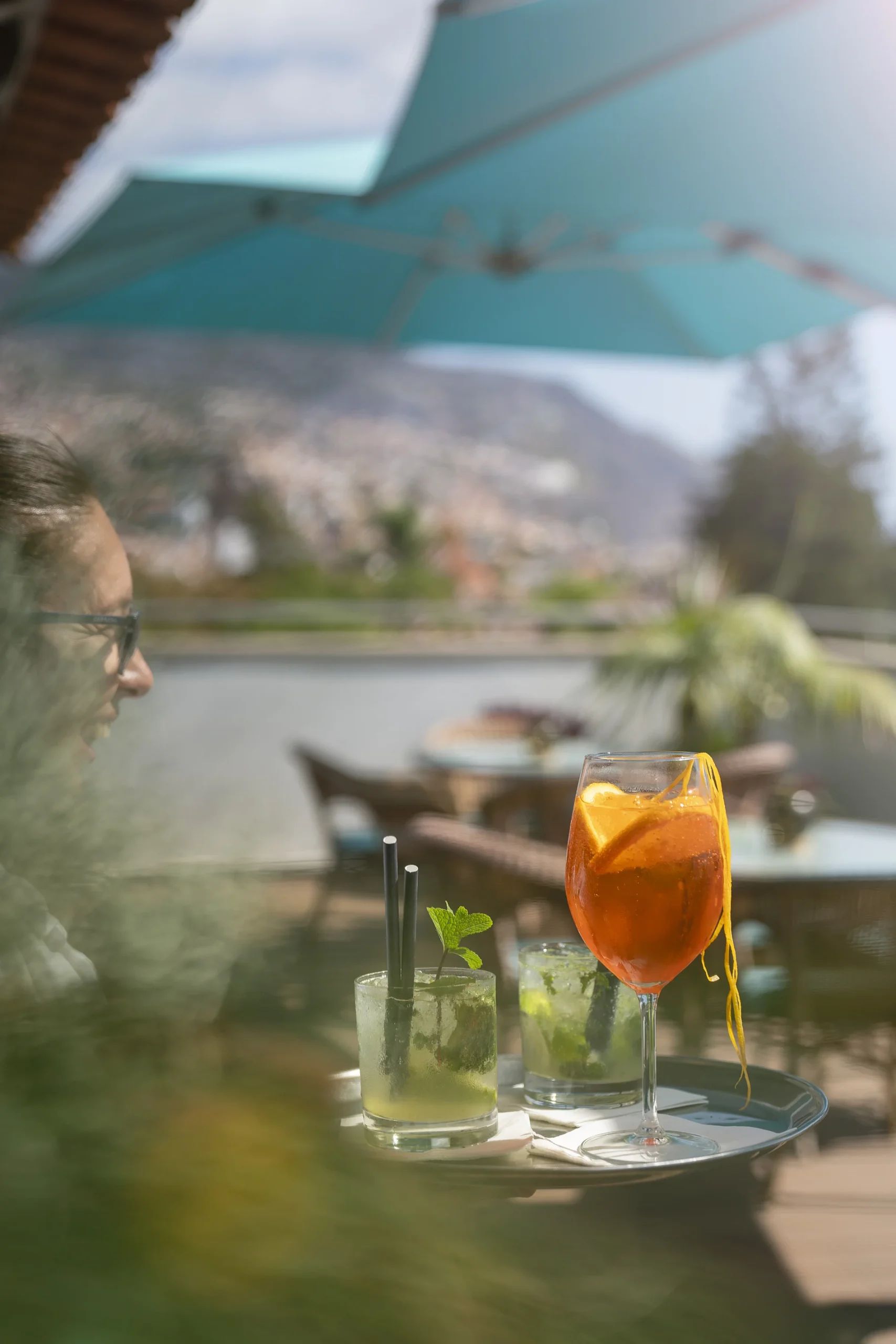 Outdoor scene with cocktails on a tray, under a blue umbrella.