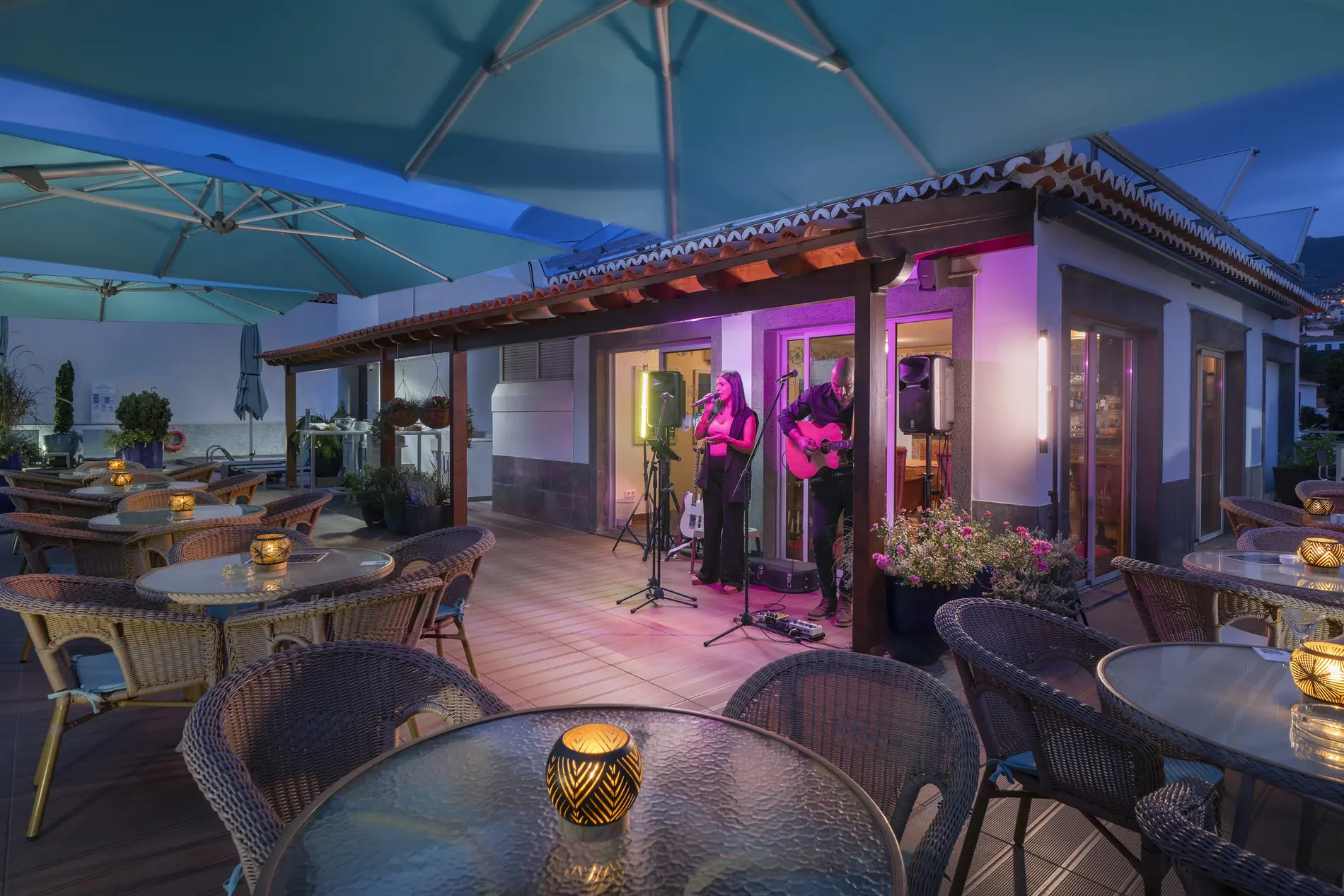 Outdoor caf&eacute; with live music performance at night, candlelit tables under umbrellas.