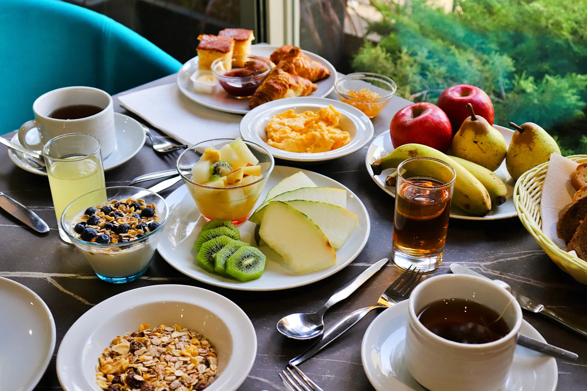 Breakfast spread with fruits, coffee, tea, juice, pastries, and yogurt.