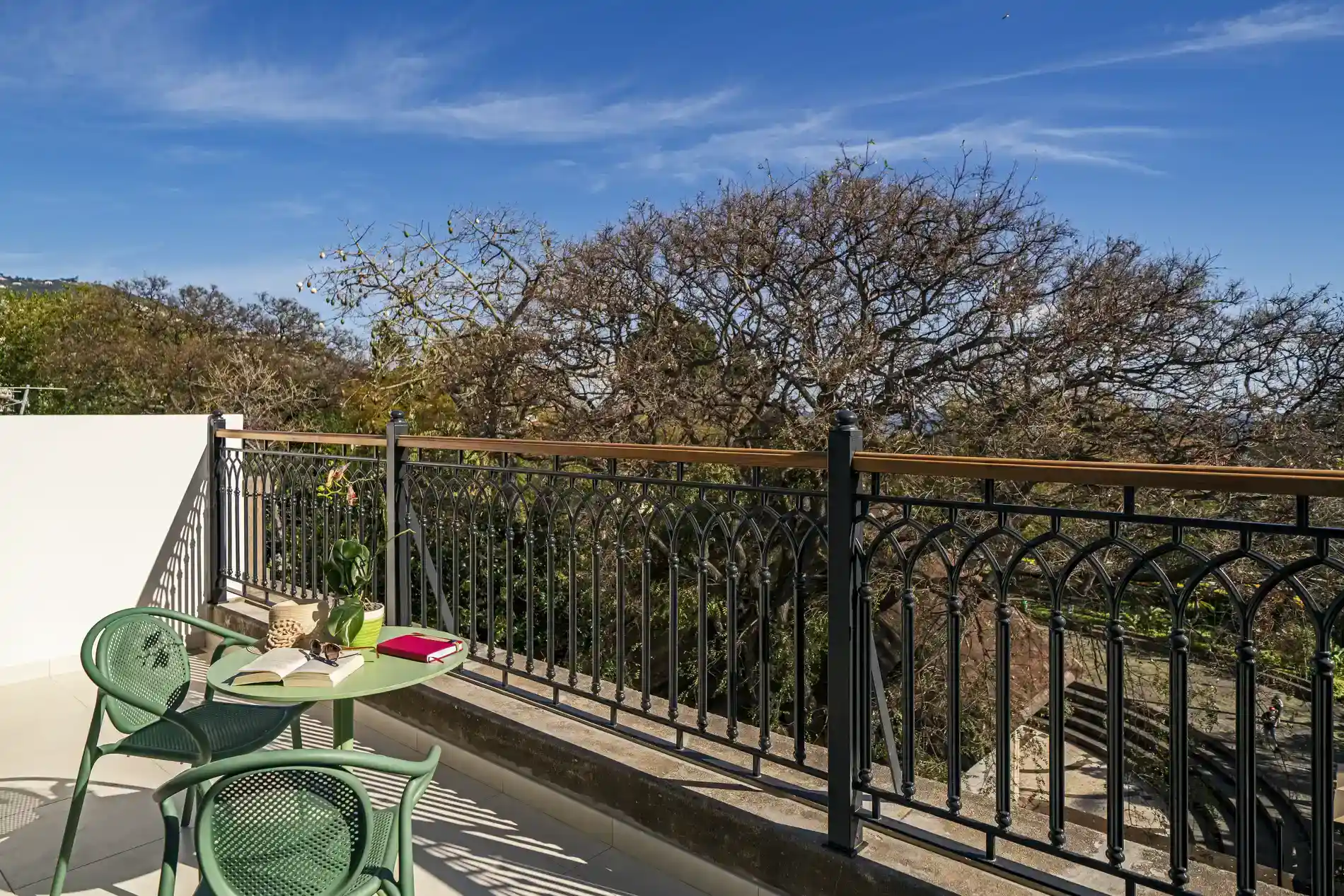 Green patio set on a balcony with trees and blue sky in the background.
