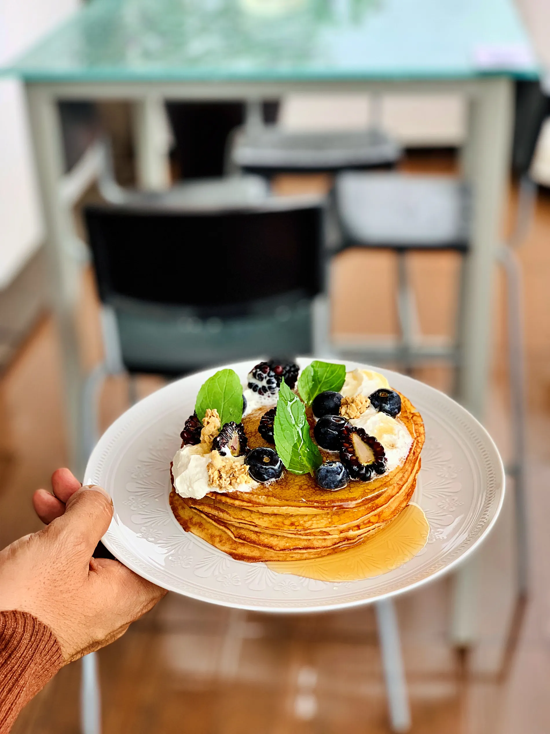 Pancakes with berries, mint leaves, and cream on a white plate.