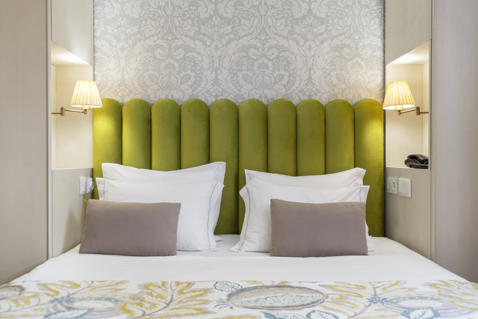 Cozy bed with green headboard, two lamps, and patterned throw.