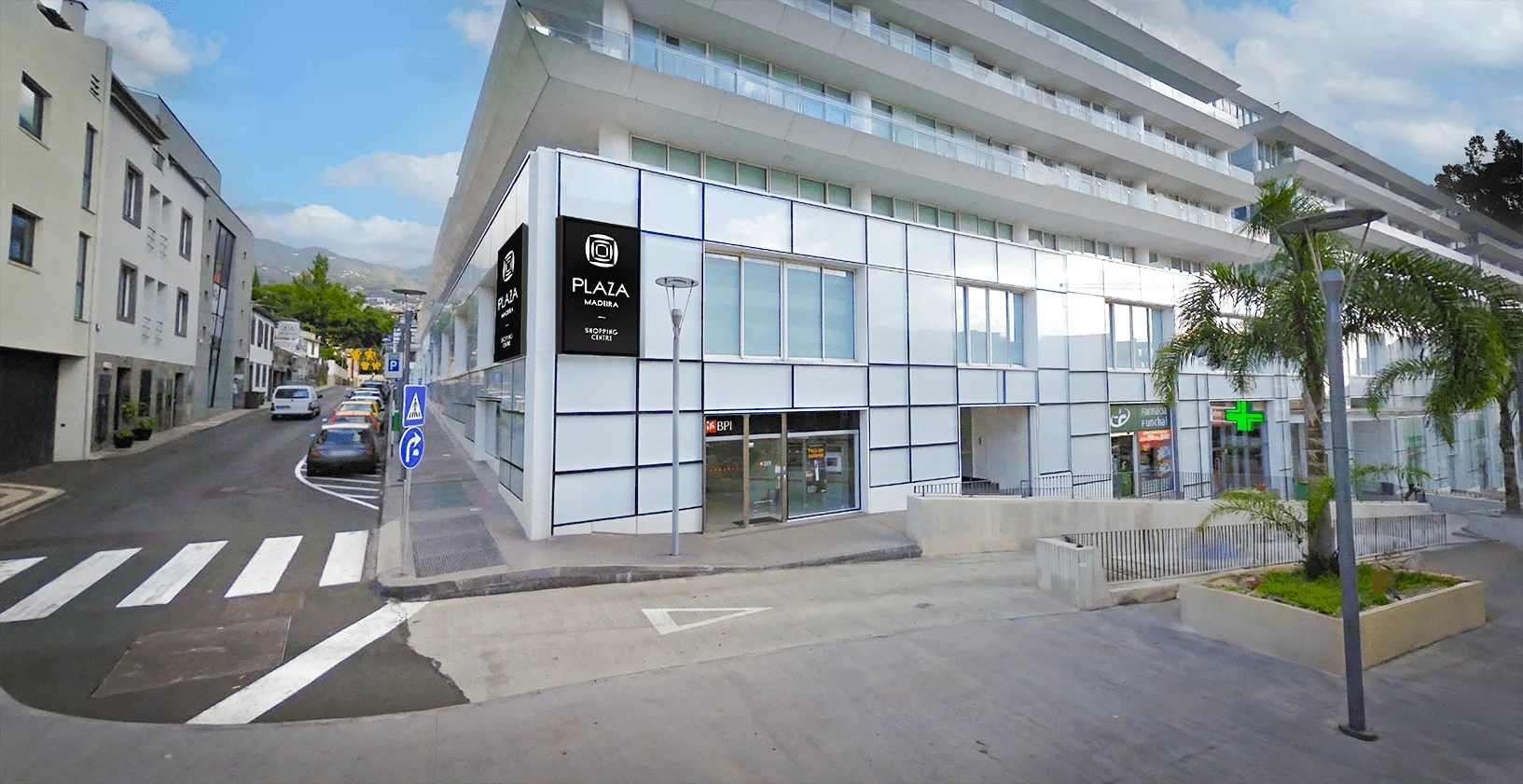 Shopping center with glass facade, palm tree, and parked cars.