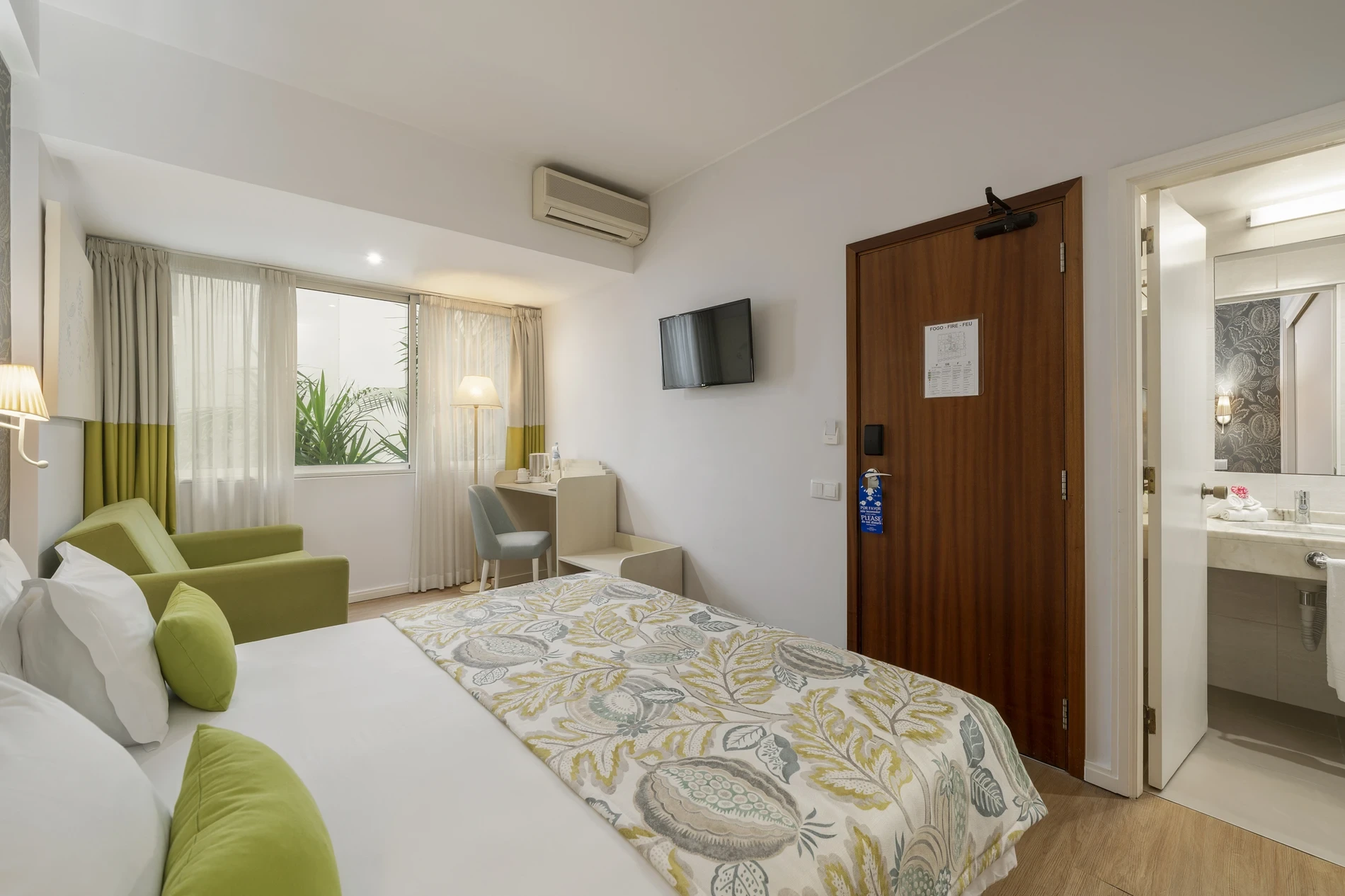 Modern hotel room with a bed, sofa, desk, TV, and bathroom access.