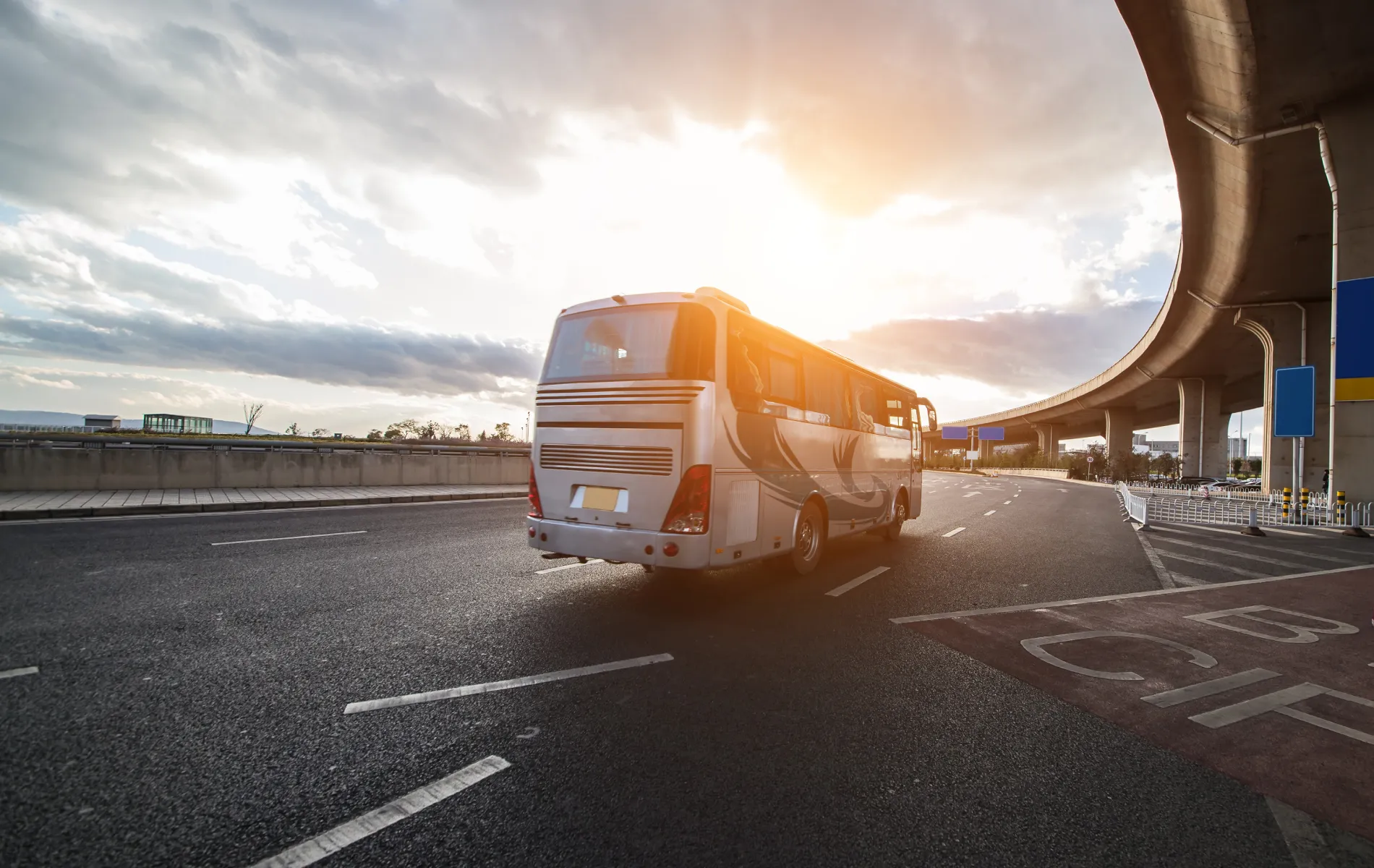 Bus driving on highway at sunset under a cloudy sky.