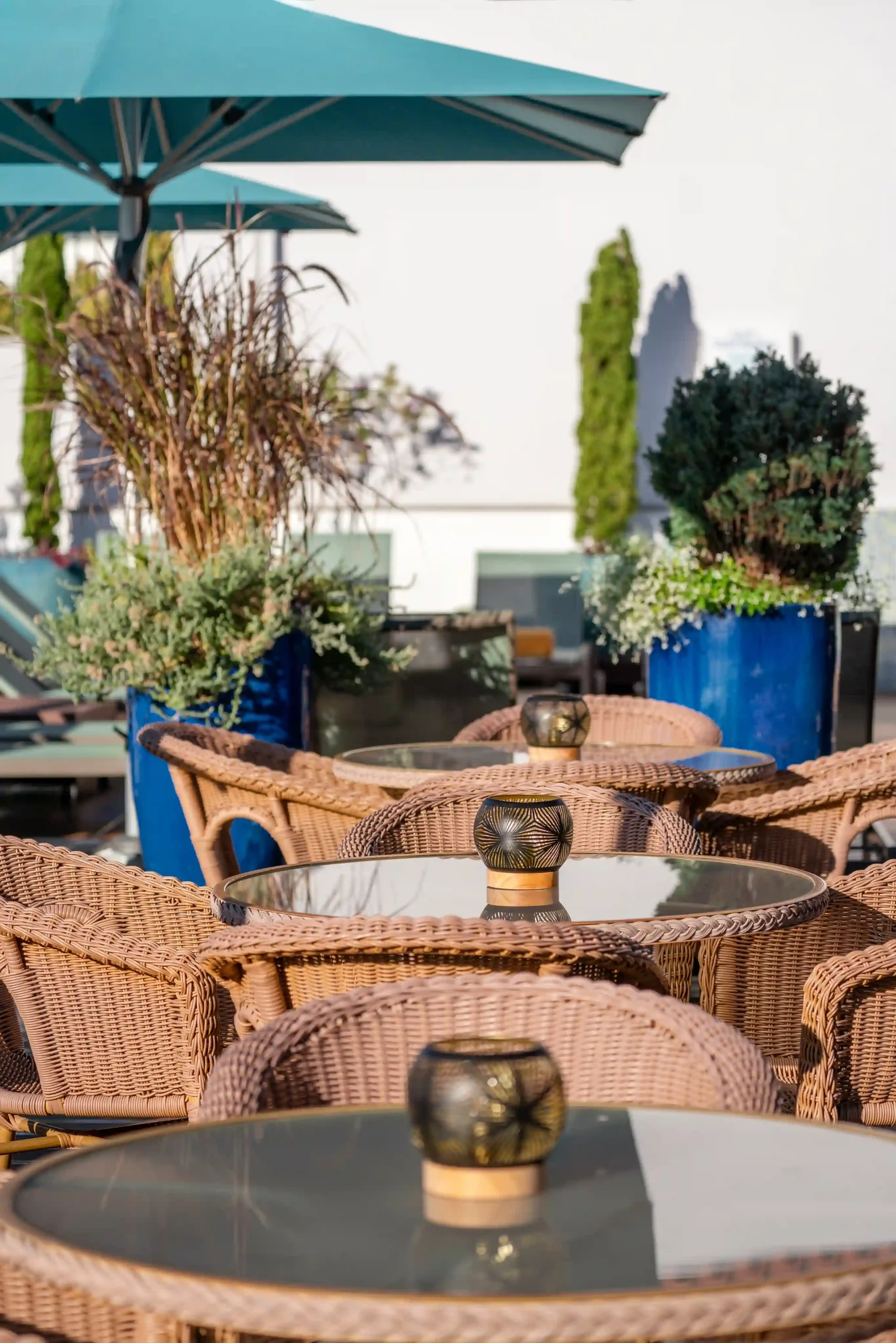 Outdoor seating with wicker chairs and glass tables under a blue umbrella.