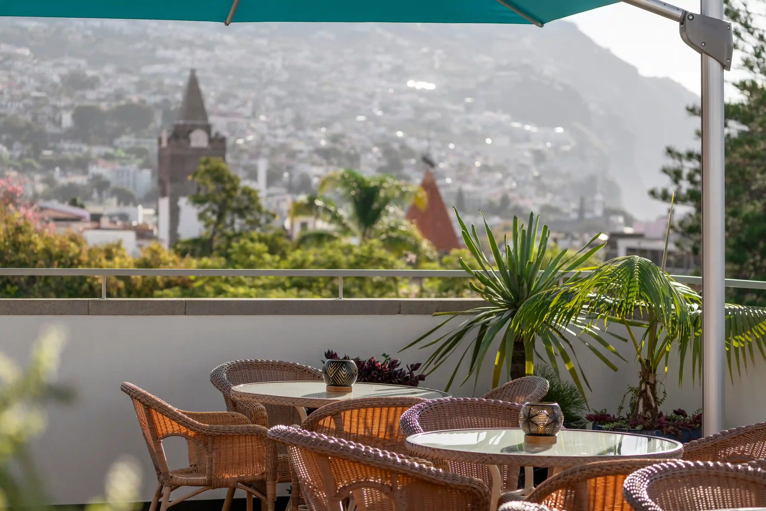 Rattan chairs and table on a patio with city view and green plants.