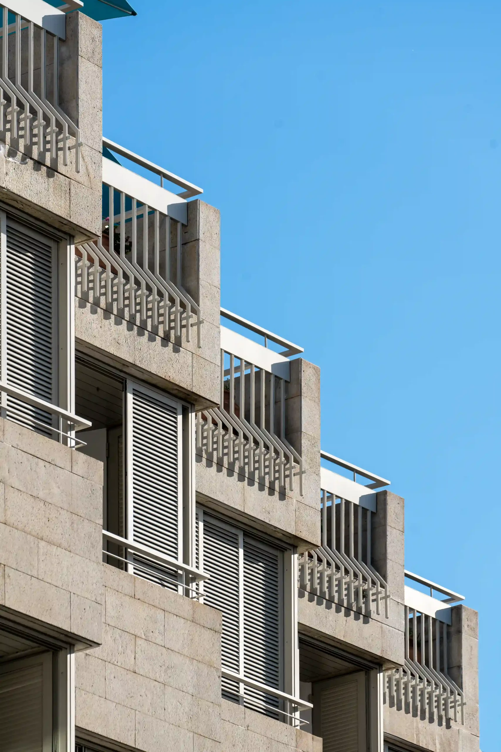 Modern beige building with balconies against a clear blue sky.