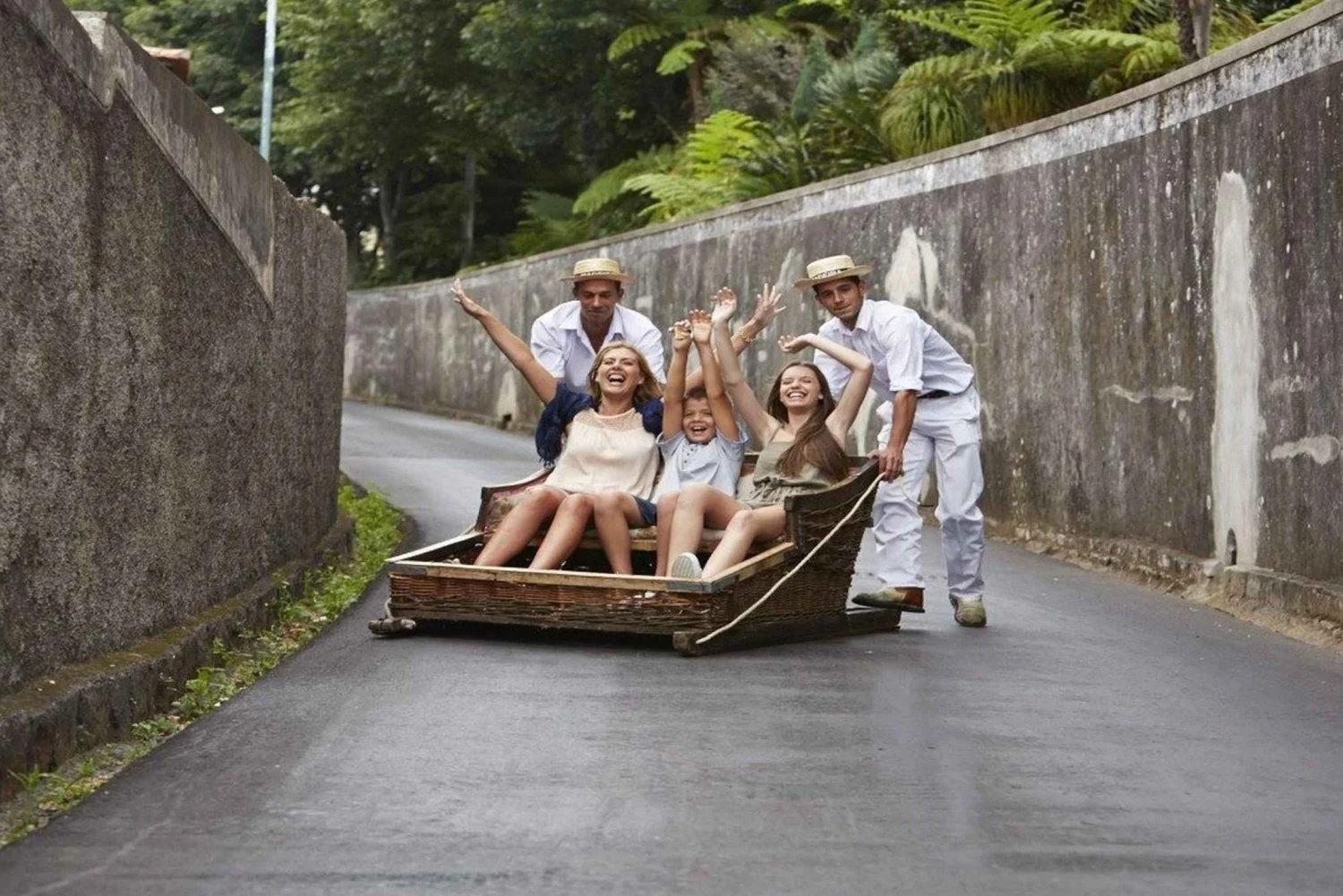 People enjoying a toboggan ride down a narrow street with drivers behind.
