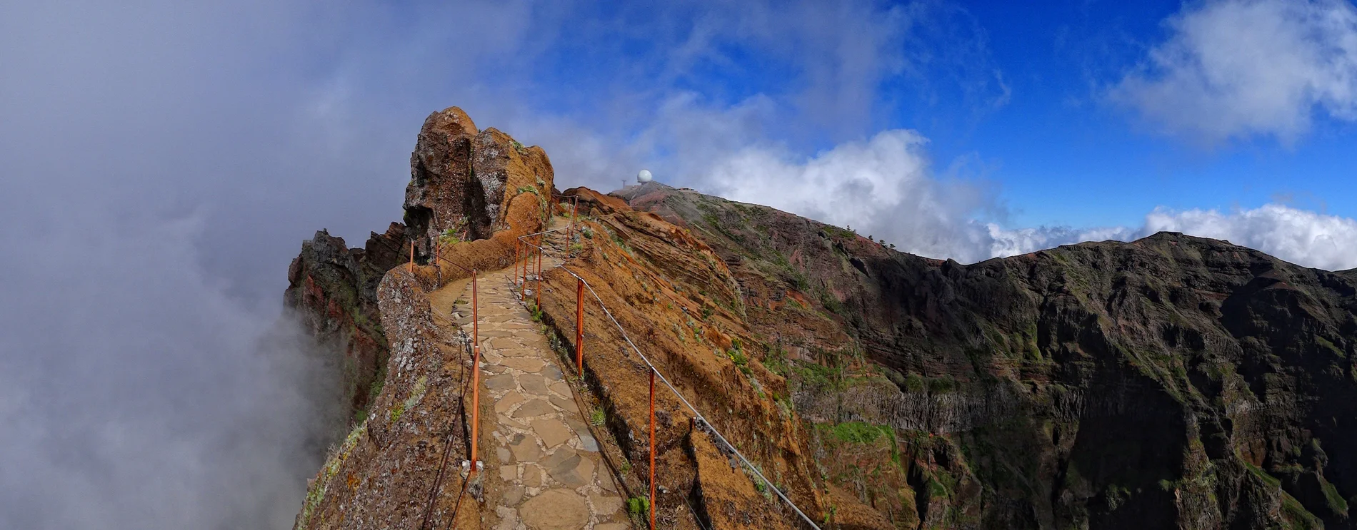 Mountain path with stone trail and dramatic cloudy sky.