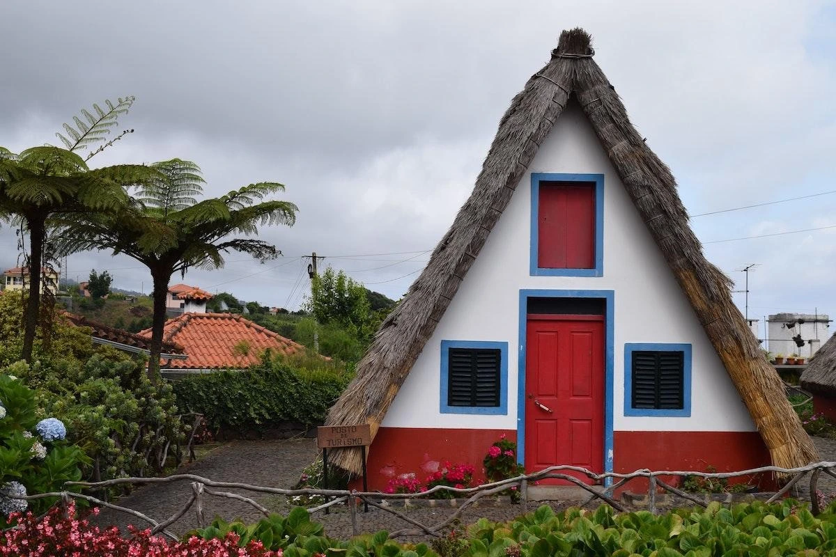 A-frame house with red doors, thatched roof, and surrounding greenery.