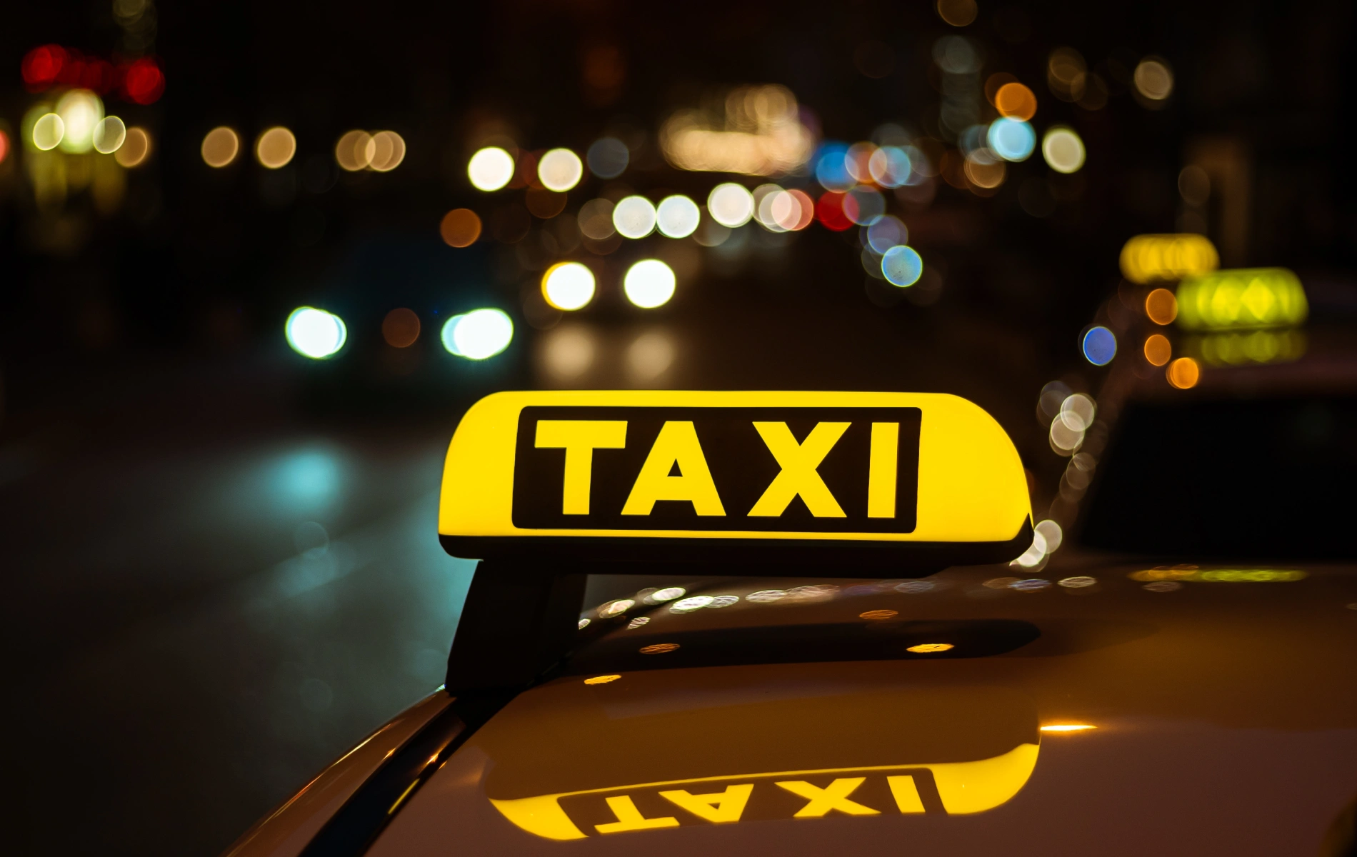 Yellow taxi sign with city lights blurred in the background.