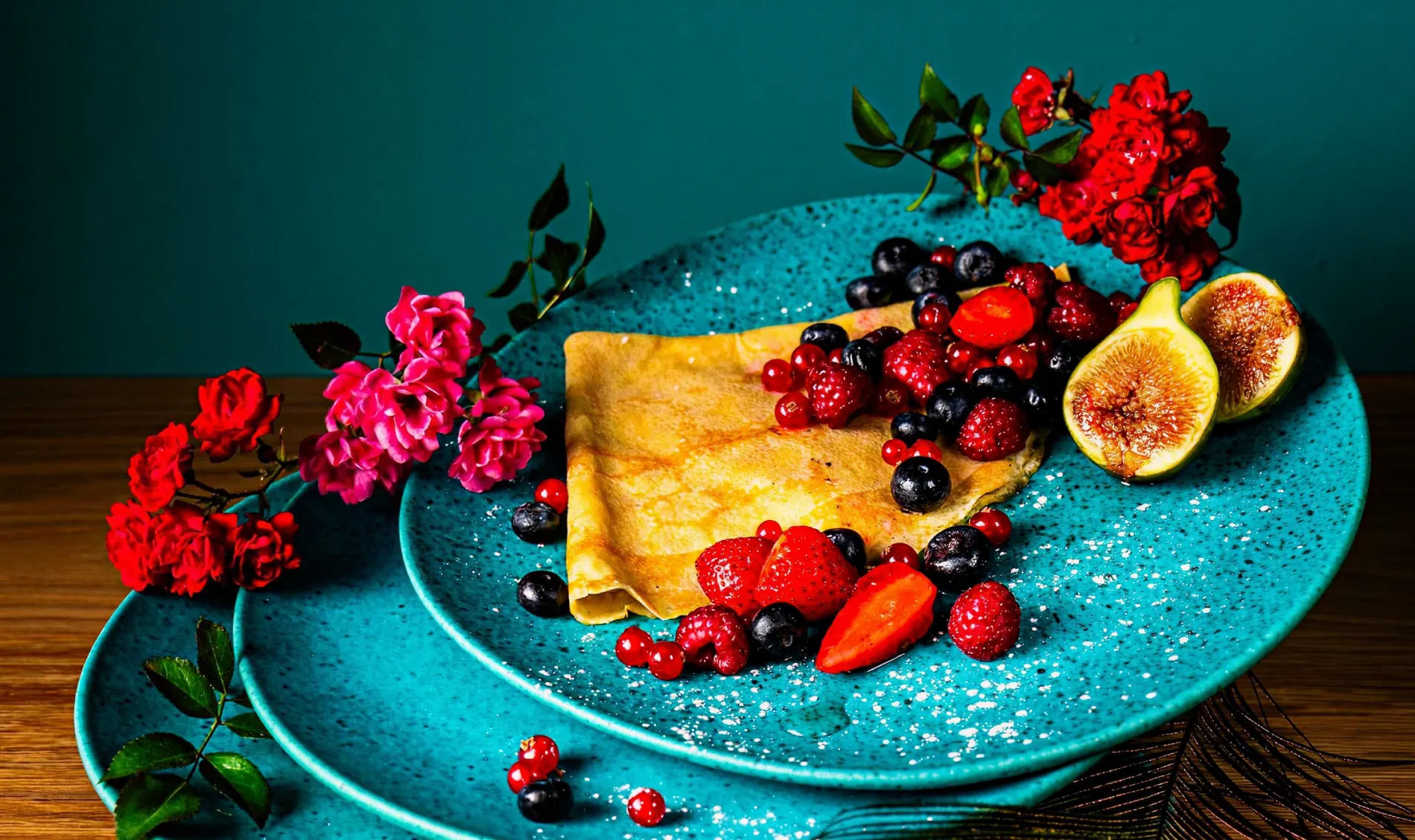 Pancake with berries, figs, and roses on a blue plate.