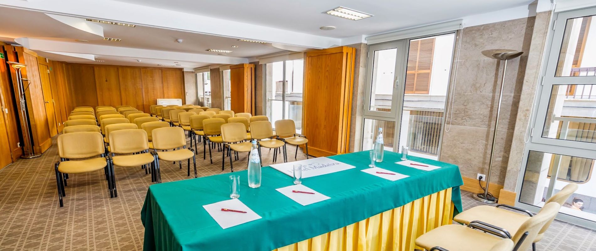 Conference room with rows of beige chairs and a panel table.