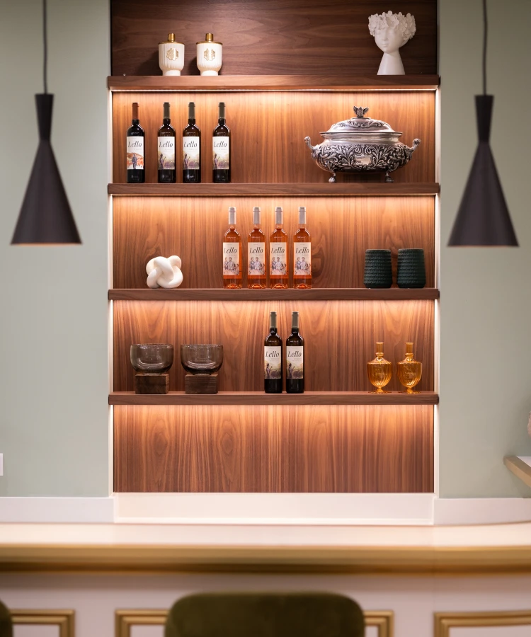 Prateleira iluminada com garrafas de vinho, ta&ccedil;as e decora&ccedil;&atilde;o elegante.