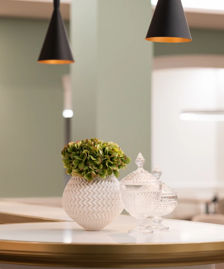 Vaso branco com flores verdes e potes de vidro sobre mesa.