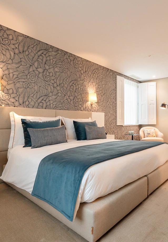 Quarto moderno com cama grande, parede floral e janela branca.