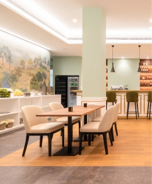 Espa&ccedil;o interno com mesas, cadeiras e balc&atilde;o de bar ao fundo.