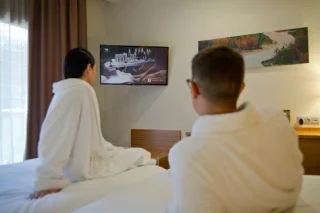 Personas en batas mirando la televisi&oacute;n en una habitaci&oacute;n de hotel.
