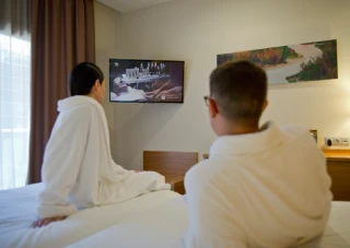 Personas en batas mirando la televisi&oacute;n en una habitaci&oacute;n de hotel.
