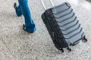 Persona con maleta negra en piso de m&aacute;rmol.