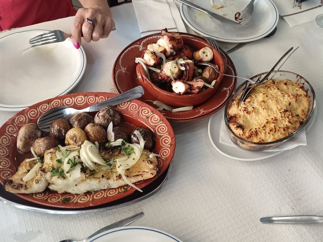 Pratos de polvo, bacalhau com batatas e gratinado sobre mesa posta em restaurante.
