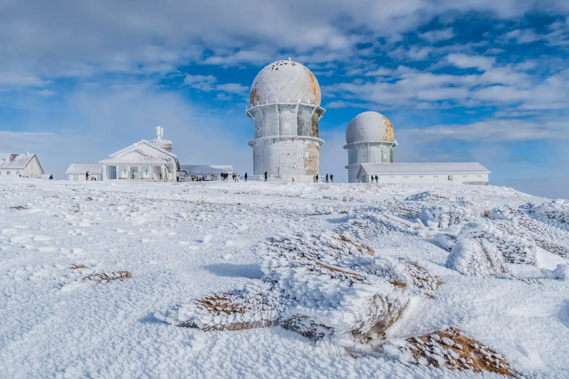 Observat&oacute;rio coberto de neve em paisagem montanhosa sob c&eacute;u azul.