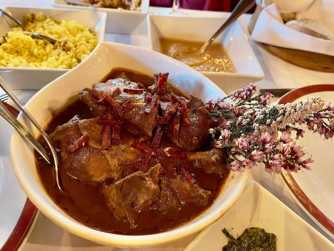 Prato de carne ensopada com arroz amarelo, molho e flores decorativas em volta.