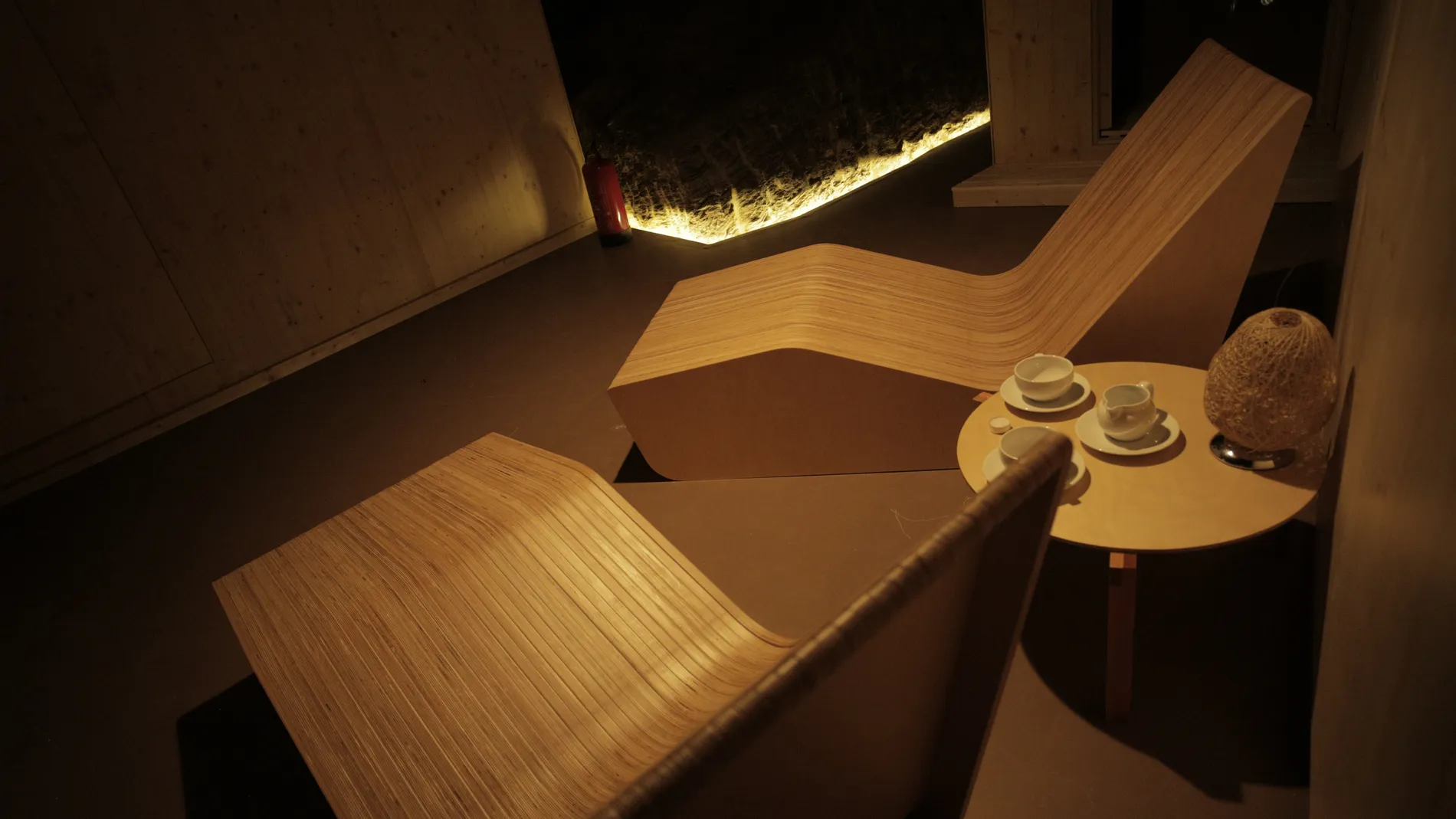 Cadeiras de madeira e mesa com lou&ccedil;a em ambiente de ilumina&ccedil;&atilde;o suave.