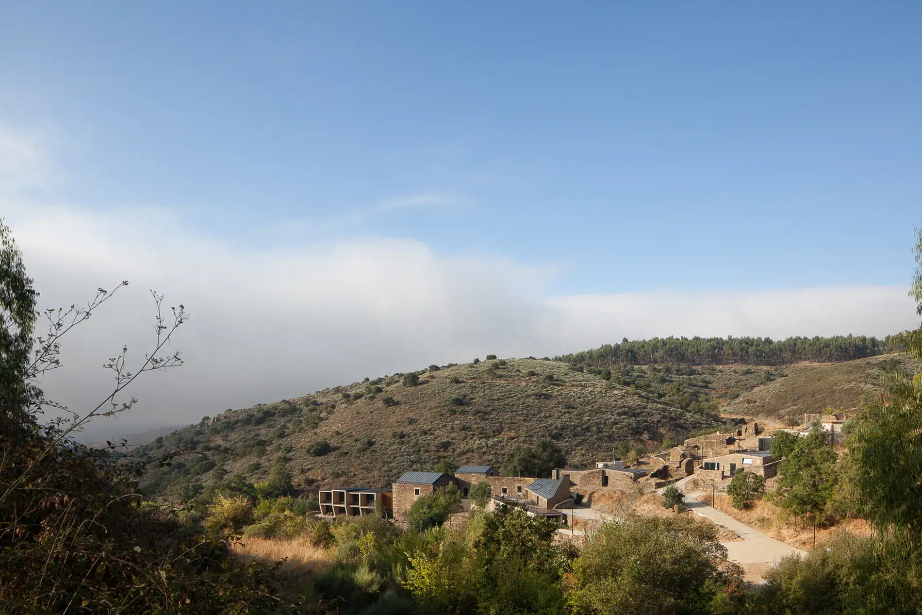 Paisagem de colinas com pequenas casas e vegeta&ccedil;&atilde;o sob c&eacute;u azul.