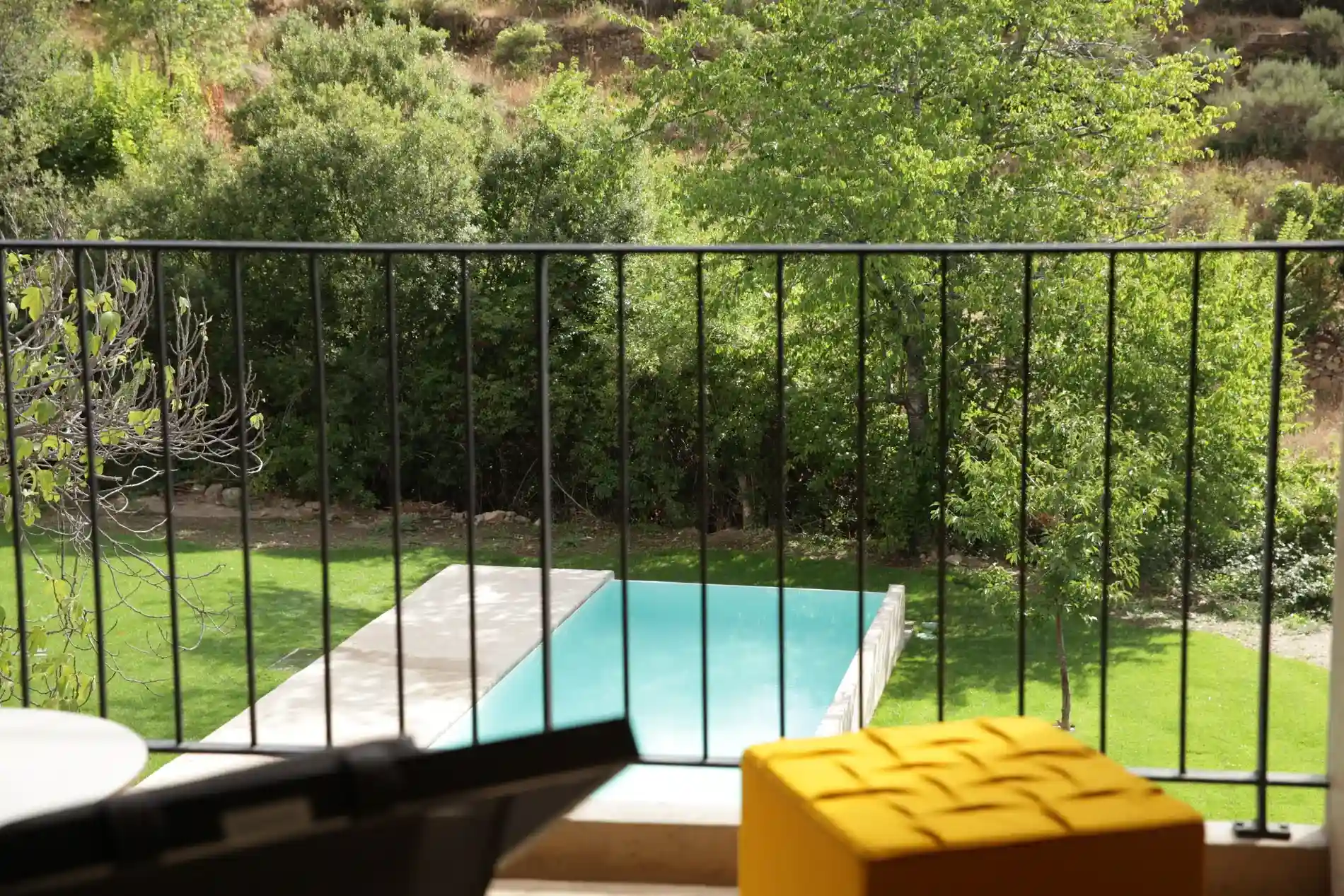 Varanda com vista para piscina, gramado e &aacute;rvores ao fundo, com item amarelo em primeiro plano.