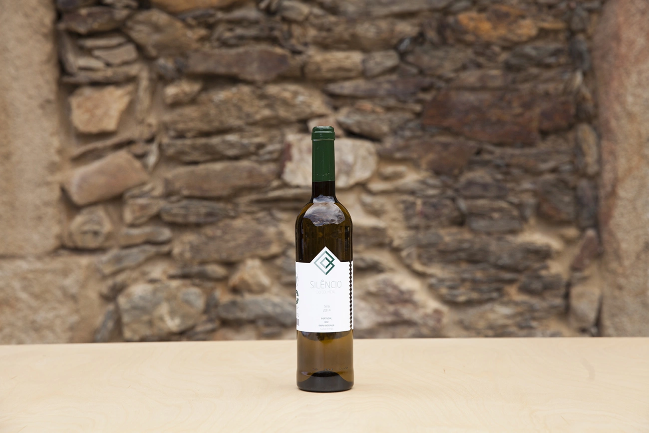 Garrafa de vinho sobre mesa, com parede de pedras ao fundo.