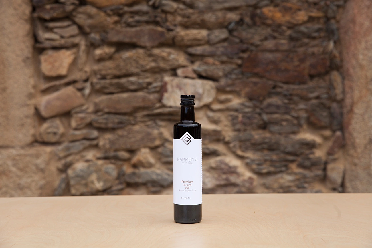 Garrafa de azeite sobre mesa de madeira, com parede de pedras ao fundo.