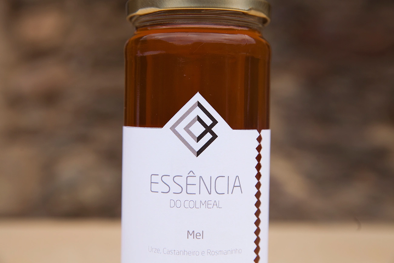 Frasco de mel "Ess&ecirc;ncia do Colmeal" com tampa dourada e r&oacute;tulo branco.