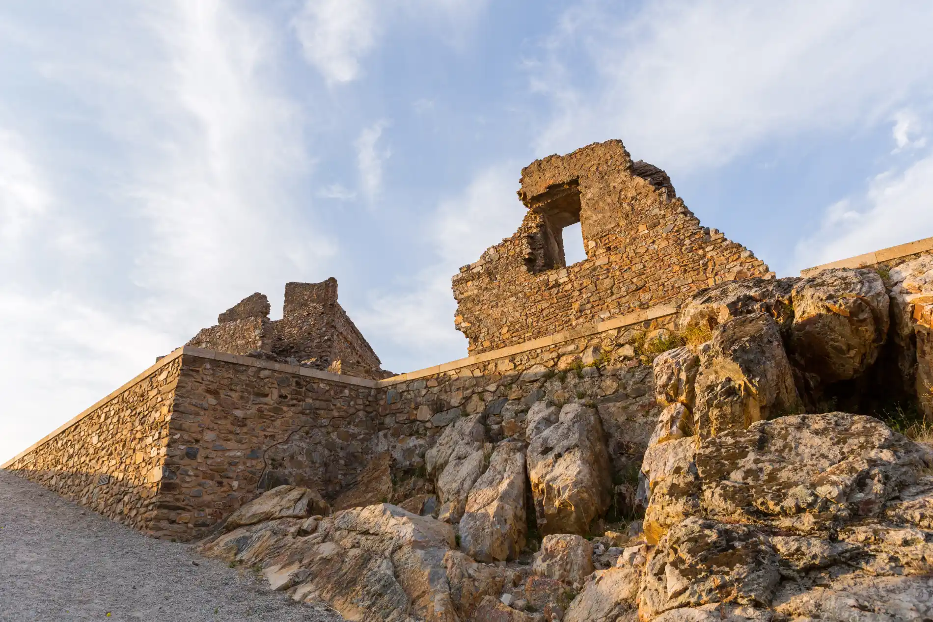 Ru&iacute;nas de uma constru&ccedil;&atilde;o de pedra sob um c&eacute;u azul com nuvens leves.